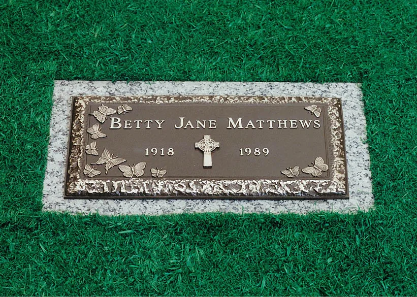 A single bronze marker with a cross and border, on a granite foundation set flush with the lawn