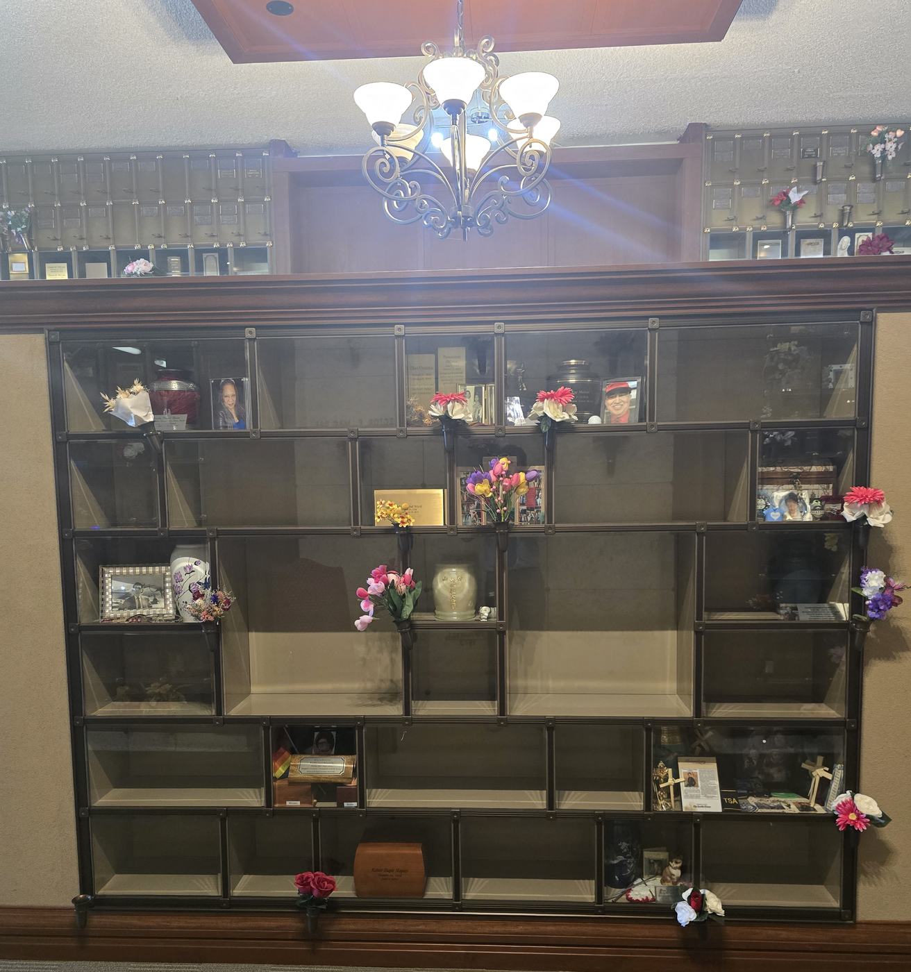 A broad face of the Eternal Light Columbarium seen straight on: rows of glass-front niches in bronze frames, many of them empty, with a chandelier above and further niche walls behind