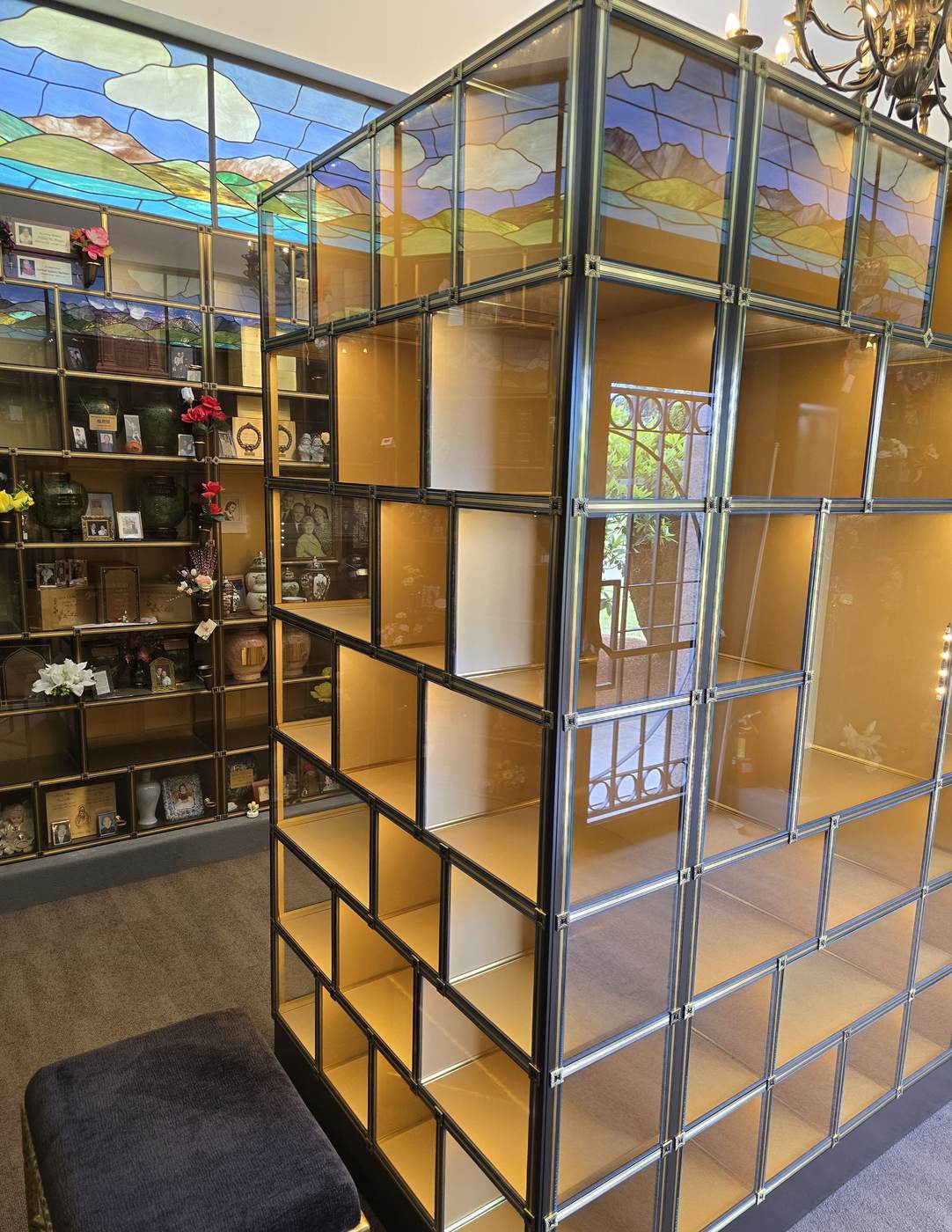 A close view along the long face of the new island: rows of empty glass niches in different widths and heights, each interior lit, with the older columbarium niches on the wall behind