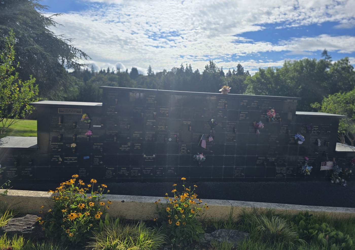 The Garden of Meditation wall in summer, seen across a planted bed of black-eyed Susans and ornamental grasses, with cedar and fir behind it
