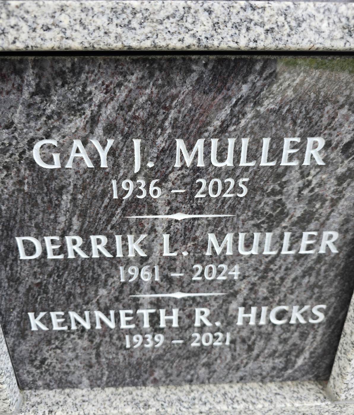 Close view of an engraved granite niche front: three names and their years of birth and death cut into the polished stone in raised white lettering, framed by lighter granite