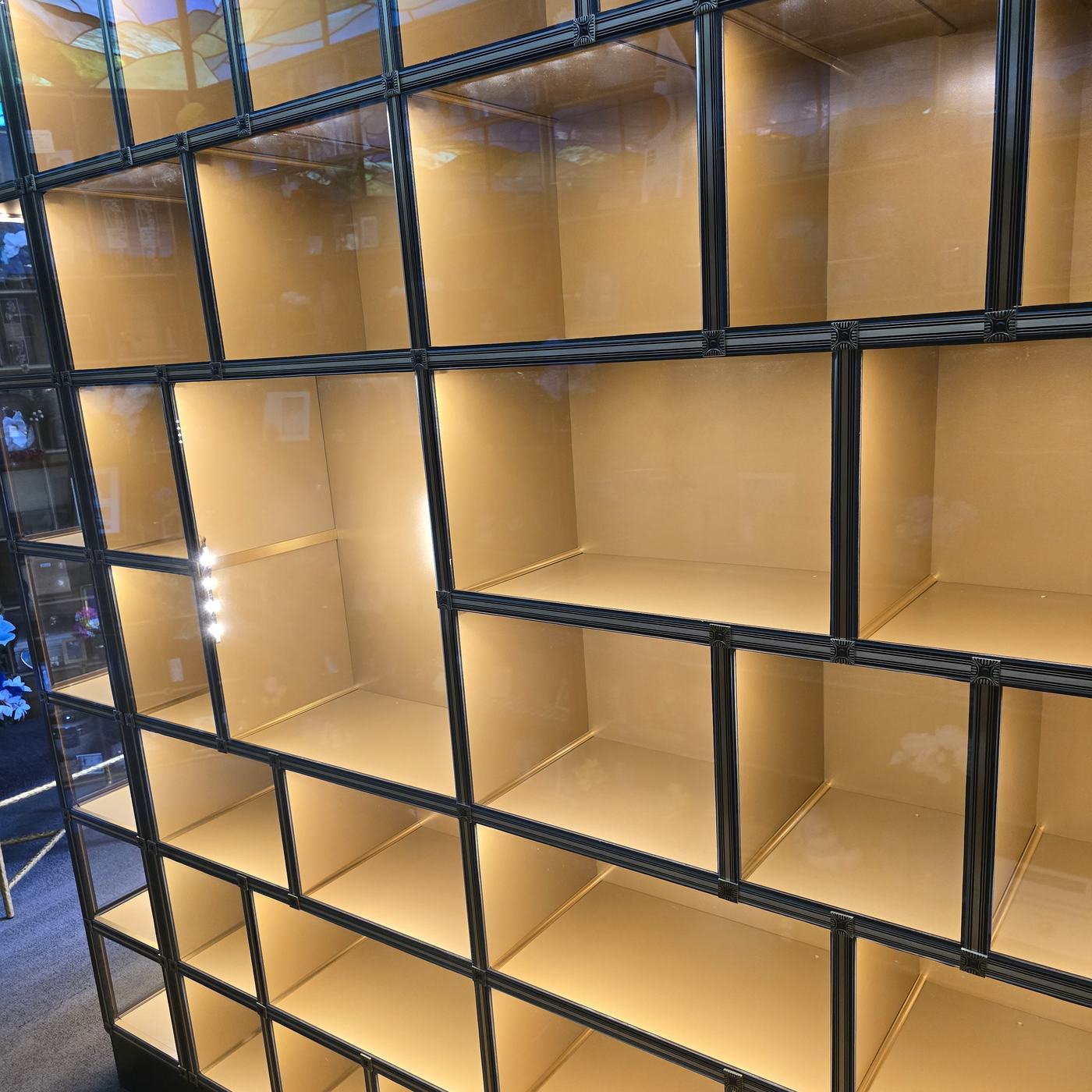 Close view of the glass-front island: several empty niches of different widths behind clear glass, each lit from within, in a black bronze frame