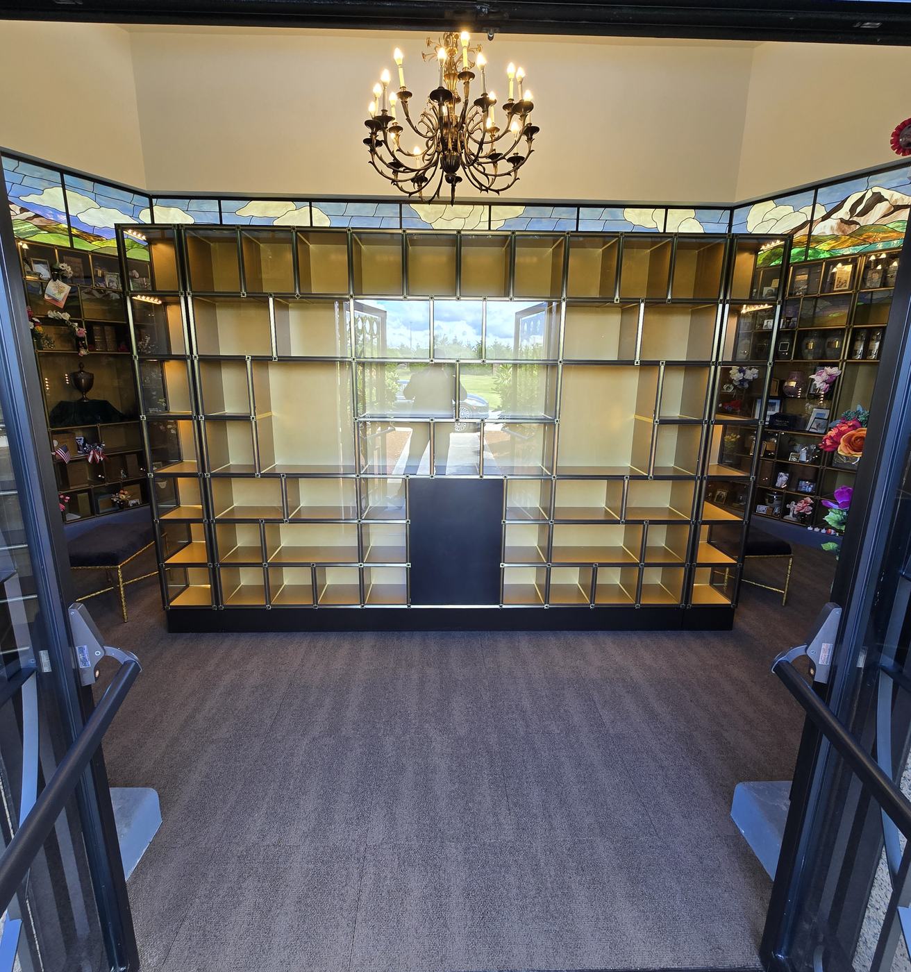 The interior of the Mountain View Columbarium seen from its doorway: an eight-sided carpeted room with a chandelier, stained-glass clerestory windows, and walls of bronze-framed glass niches on both sides of the central island