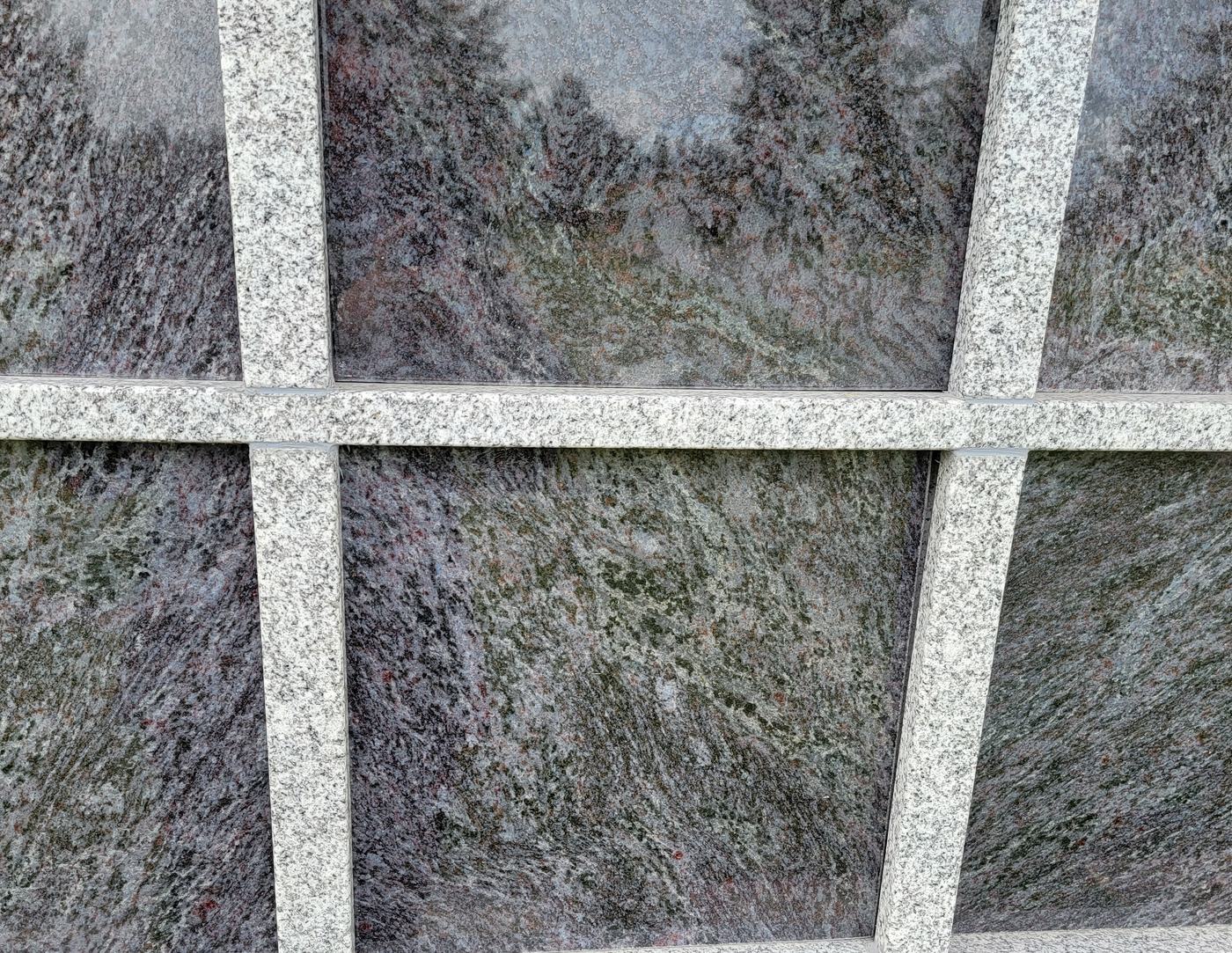 Close view of Rock of Ages niche fronts: four dark grey granite panels with pale swirling grain, set in a pale speckled granite frame